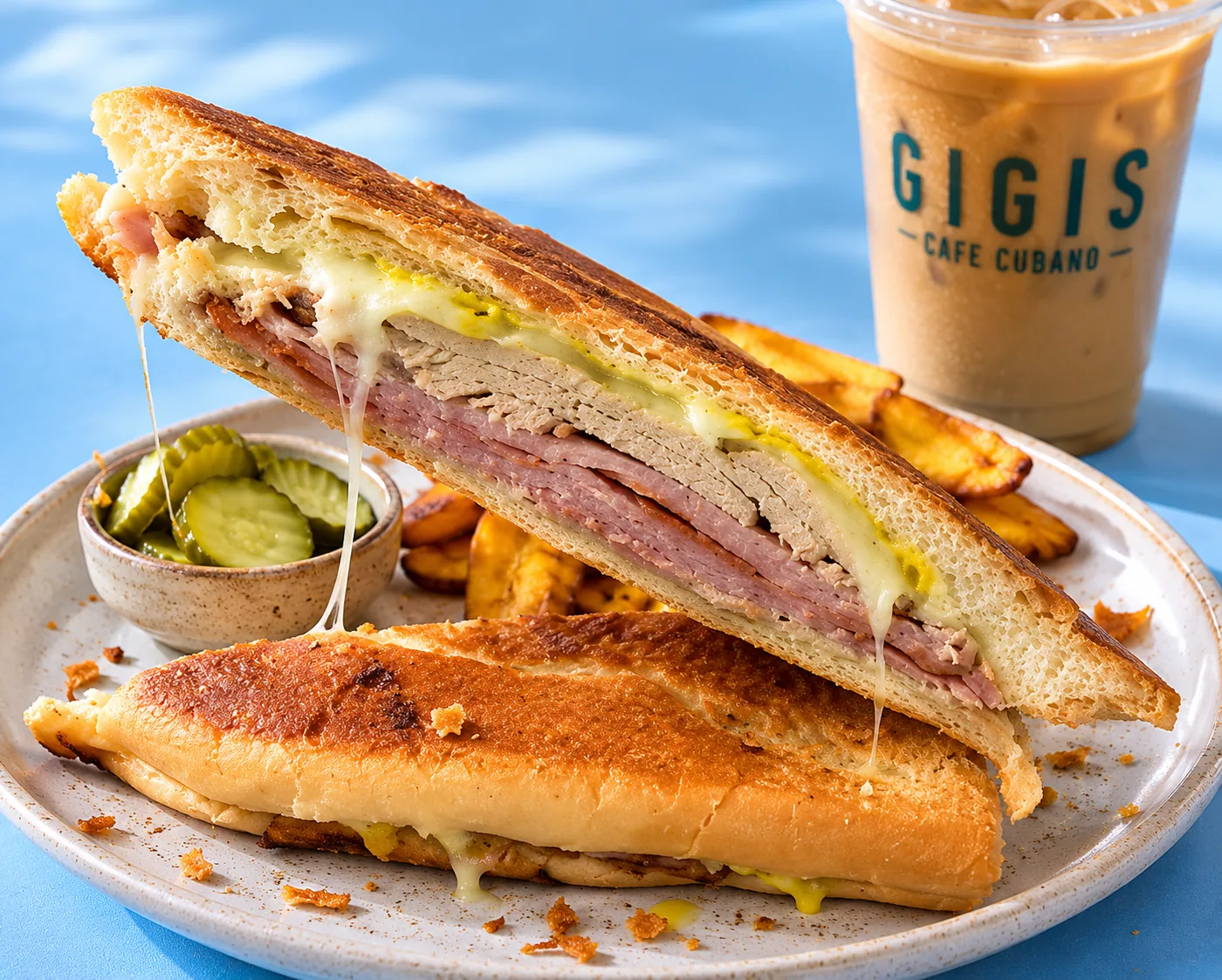 A pressed GIGIS Cubano cut in half, served with plantain chips, pickles and an iced café con leche